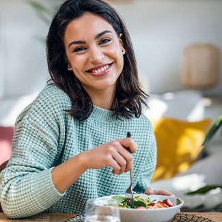 Woman in green sweater sitting at table forking salad