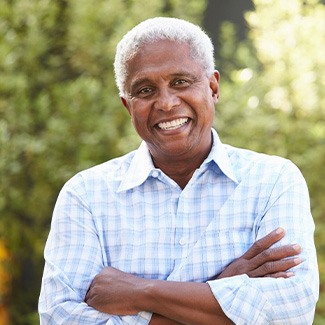 Man in blue checkered shirt outside with arms crossed smiling