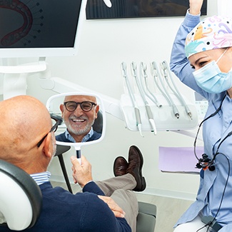 Older man pleased with smile he sees in the mirror at dentist’s office