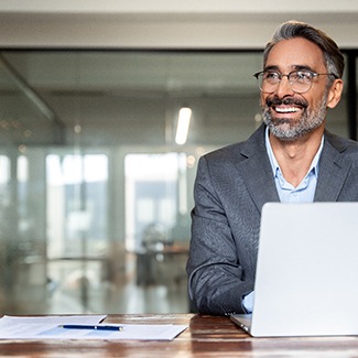 Middle-aged man in suit sitting and smiling at laptop