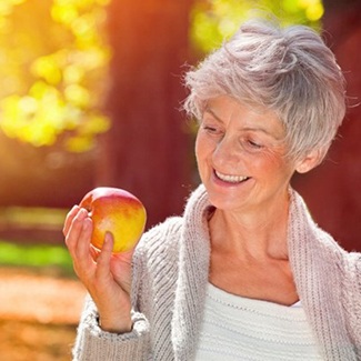 Woman with dental implants in Dallas smiling at apple
