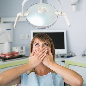 young woman holding her mouth in fear in the dental chair 