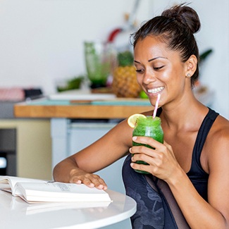 Smiling woman drinking green juice while reading