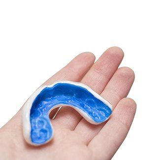 Patient holding blue and white mouthguard in palm of hand