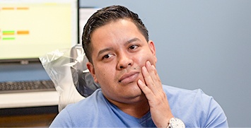 Male dental patient in dental chair holding cheek in pain