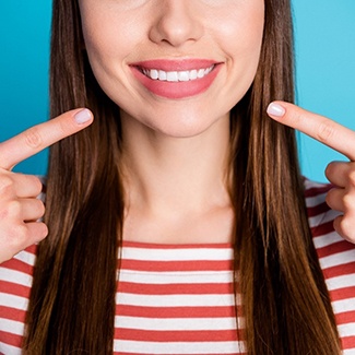 An up-close view of a young woman pointing toward her mouth to show off her new veneers