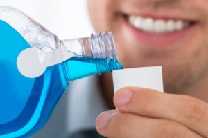 Smiling man with healthy teeth pouring blue mouthwash into cup