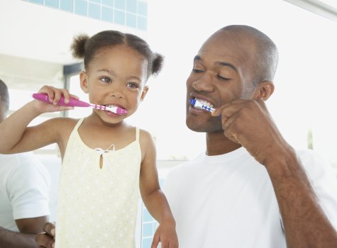 parent showing child how to brush teeth
