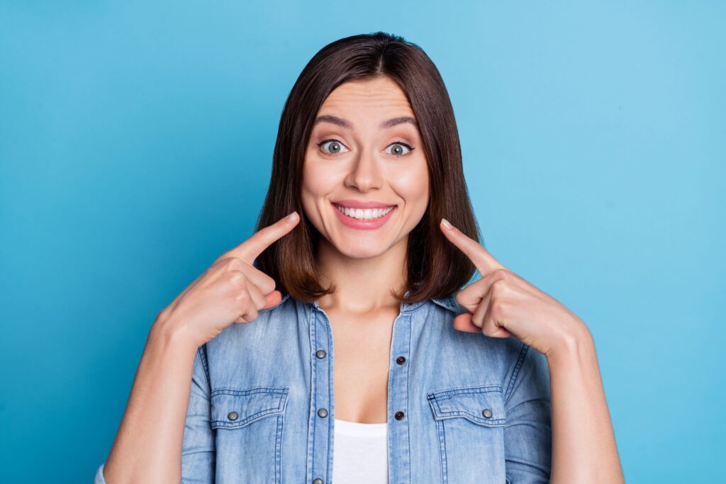 Woman in denim shirt pointing to her smile with two fingers