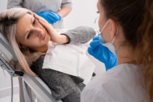 Woman holding jaw in pain in dentist's chair. 
