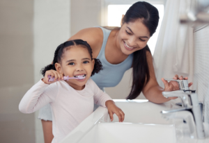 a child brushing her teeth under her mom’s supervision