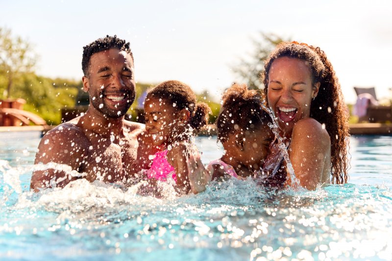 Family with good oral health smiling and splashing in pool